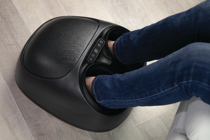 Person's feet inserted into a sleek black electric foot massager for relaxation.