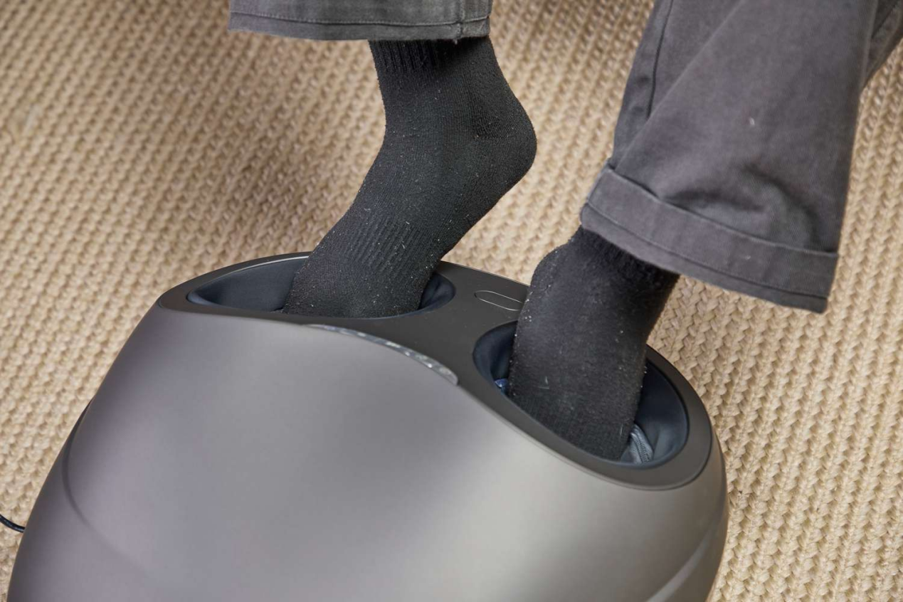 Feet in black socks enjoying a relaxing grey foot massager on a carpet.